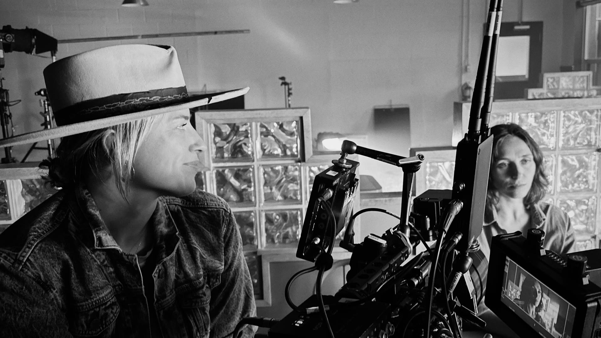 Angelia Hughes in her flat-brim hat watching a take from beside the camera, the actor visible on the monitor.